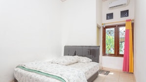 A bedroom with a bed, a window with curtains, and an air conditioning unit. - Griyaponcowolo (Yogyakarta)