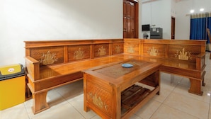 A room with a wooden bench and a matching table, a trash bin, and a door. - Griyaponcowolo (Yogyakarta)