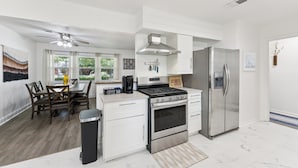 A modern kitchen with white cabinetry, stainless steel appliances, and a dining area with wooden chairs and a table. - Boho Bungalow near DFW Airport (Farmers Branch)