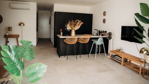 Een moderne keuken met een zwart aanrecht, twee rieten stoelen, een houten bank en een televisie aan de muur.