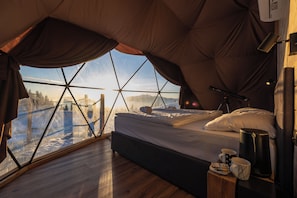 Tienda con cama, ventana y vista a un paisaje nevado.