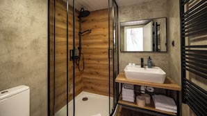 Un baño moderno con ducha envuelta en vidrio, un lavamanos blanco y un mueble de tocador de madera.