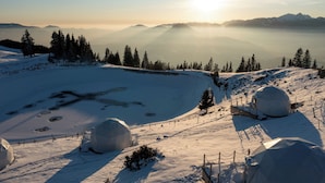 Un paisaje nevado con una estructura en forma de cúpula, probablemente una cúpula geodésica, rodeada de nieve y árboles.