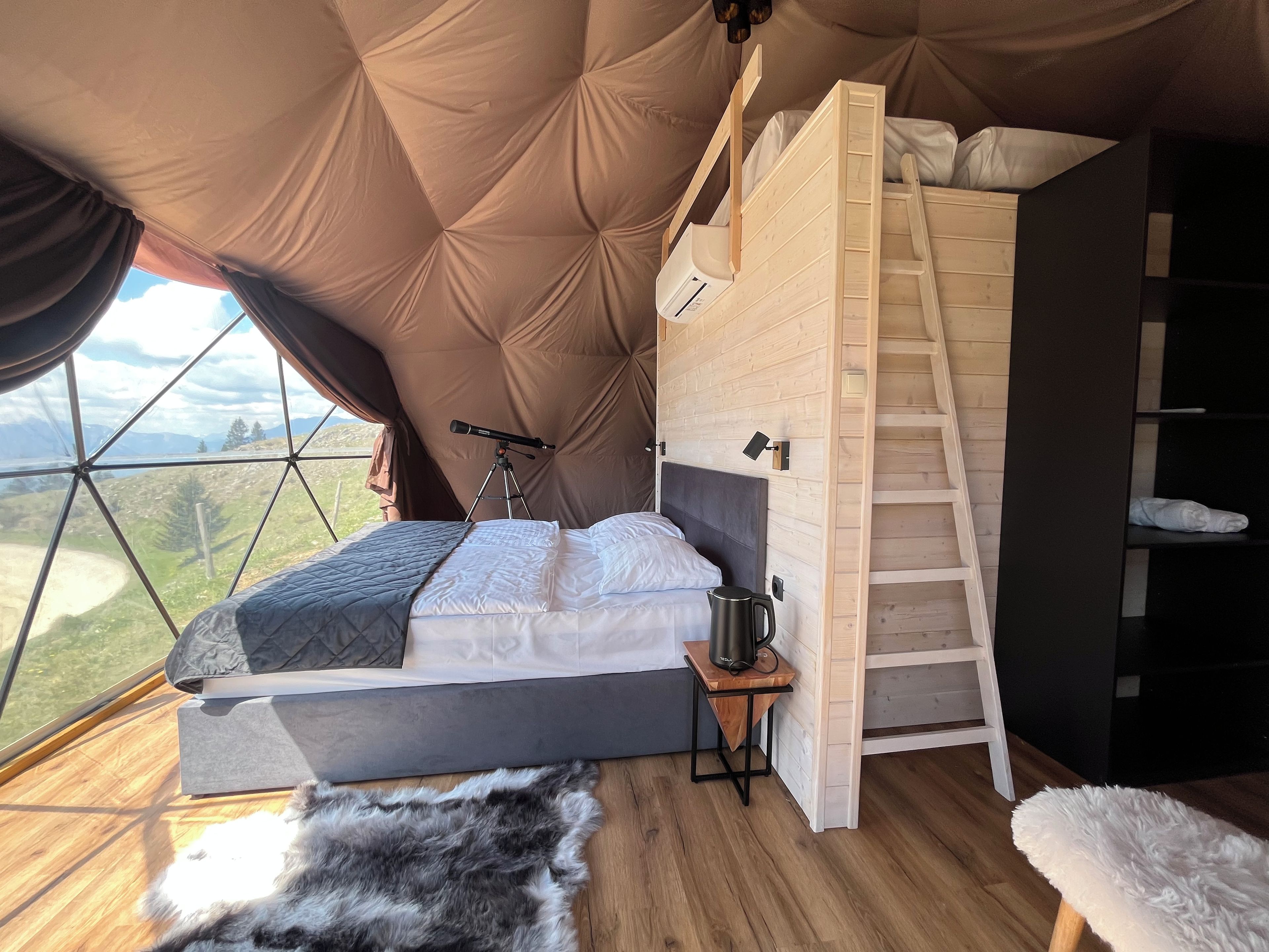 A cozy tented room with a bunk bed, a telescope, and a view of the outdoors.