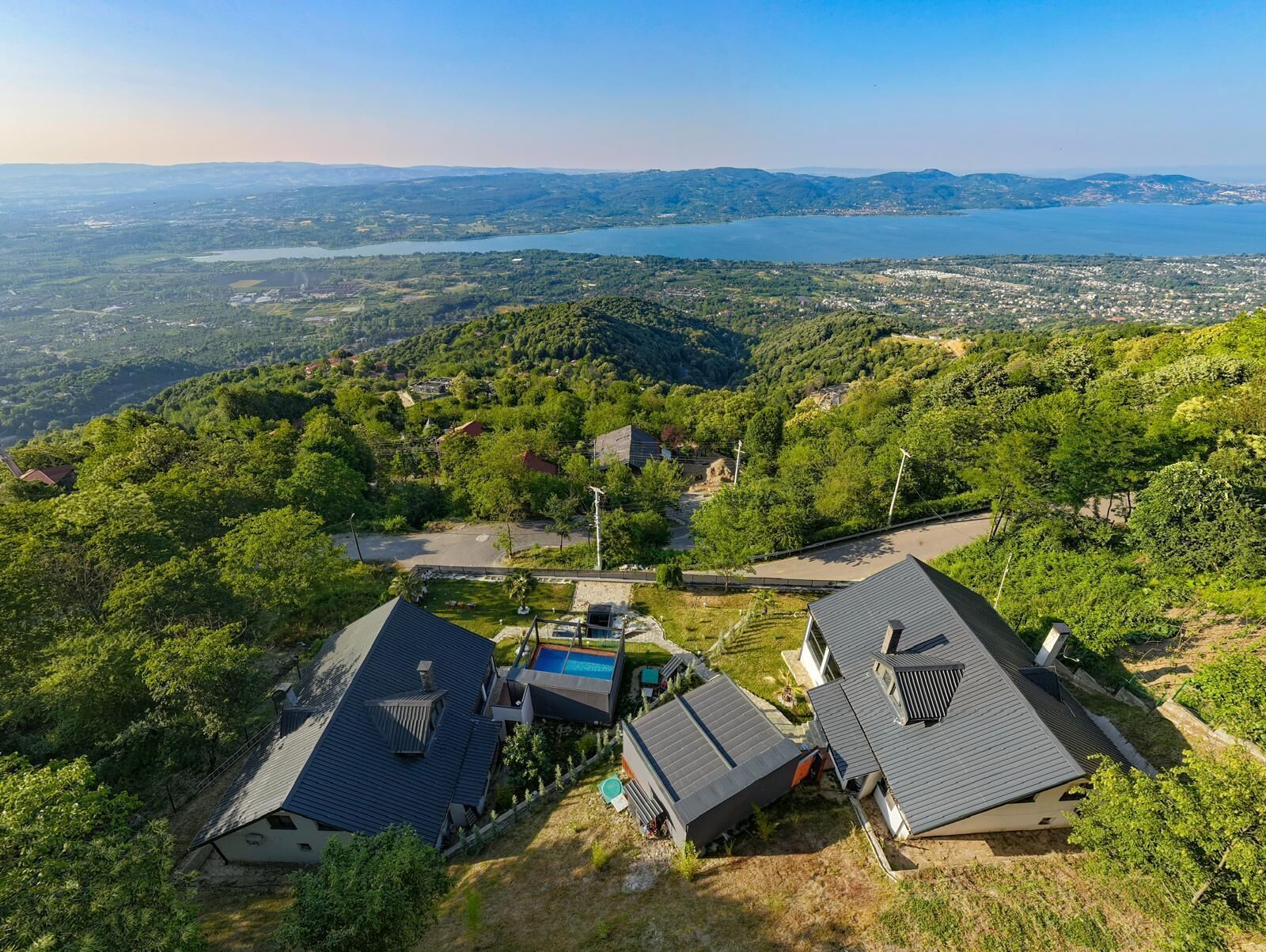 Un quartier résidentiel avec des maisons construites sur une colline, une piscine et une vue sur un lac et des montagnes lointaines.