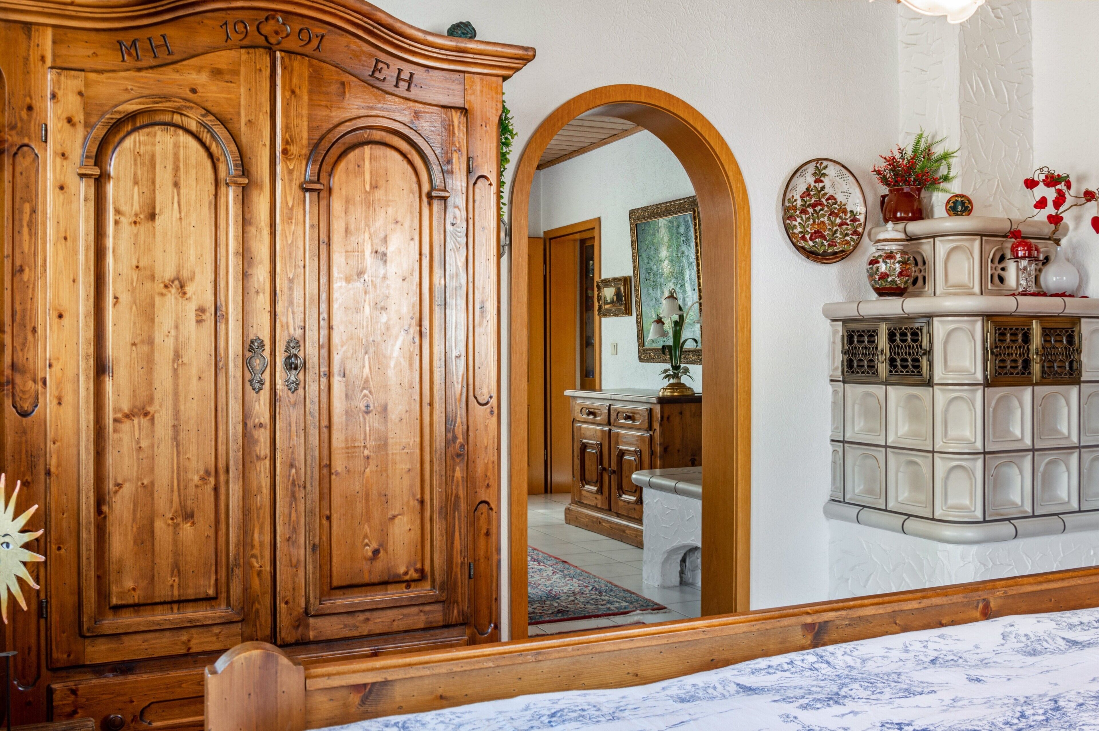 Ein Holzkleiderschrank mit Spiegel darüber, ein weiß gefliester Boden und eine weiße Wand mit dekorativen Tellern.
