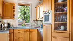 Een keuken met houten kasten, een vaatwasser, een raam met uitzicht op groen en een magnetron.