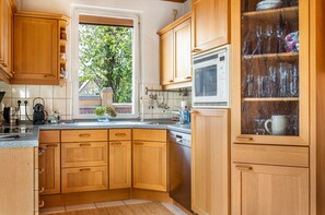 A kitchen with wooden cabinets, a dishwasher, a window with a view of greenery, and a microwave.