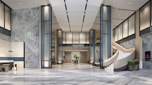 Een ruime lobby met een marmeren vloer, een centrale trap en een receptiebalie.