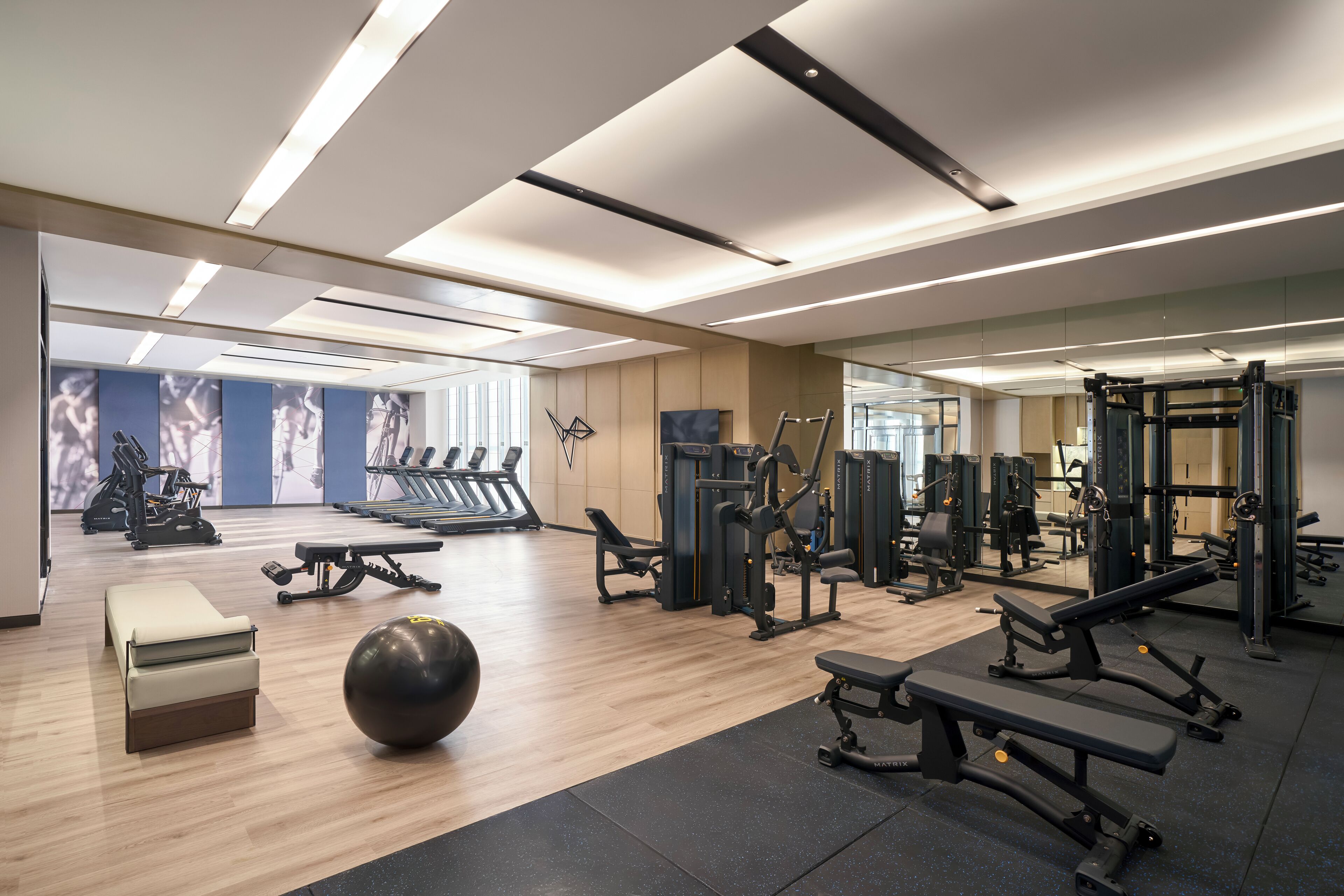 Ein modernes Fitnessstudio mit unterschiedlichen Trainingsgeräten, einem großen Spiegel und einem Holzboden.
