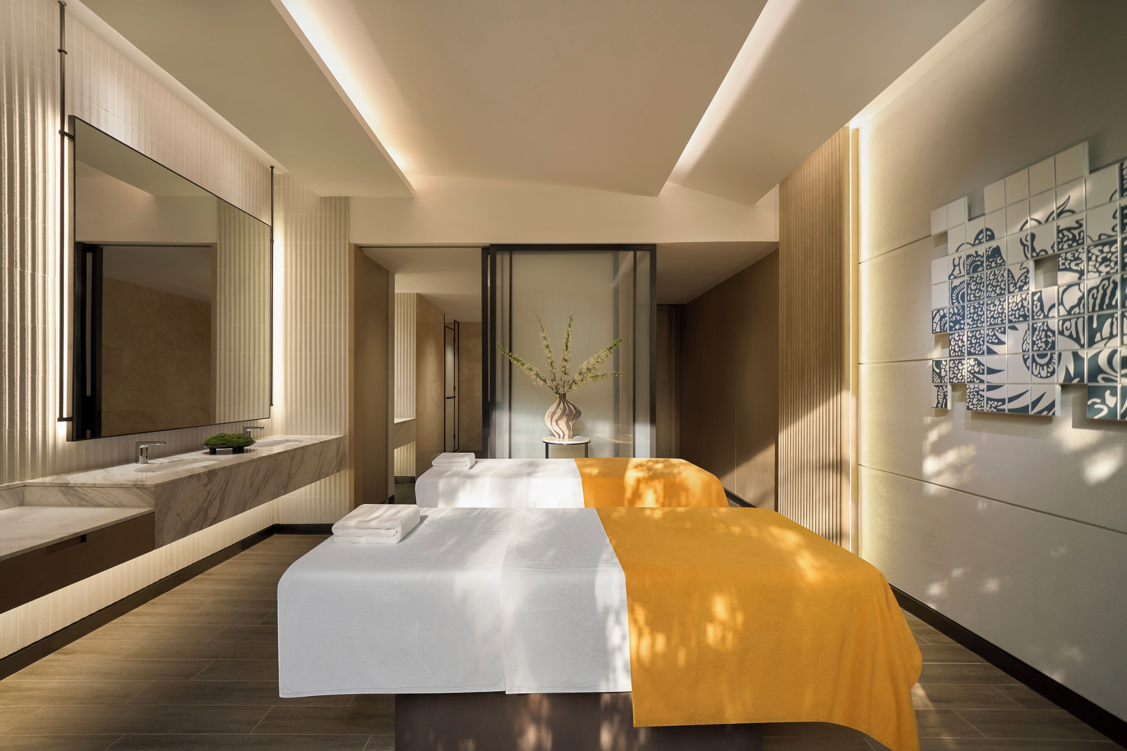 A modern hotel room with a large bed, a separate sitting area, a large mirror, and a decorative wall.