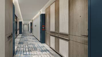 A hotel hallway with a patterned carpet, wooden walls, and a digital elevator display.