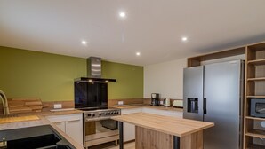 A modern kitchen with a central island, stainless steel appliances, and a green accent wall. - Spacious 8-bedroom cottage in Anjou vineyards (Blaison-Saint-Sulpice)