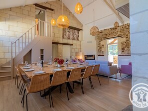 A spacious dining area with a long wooden table set for six, surrounded by wicker chairs. A staircase with a white railing leads to an upper level.