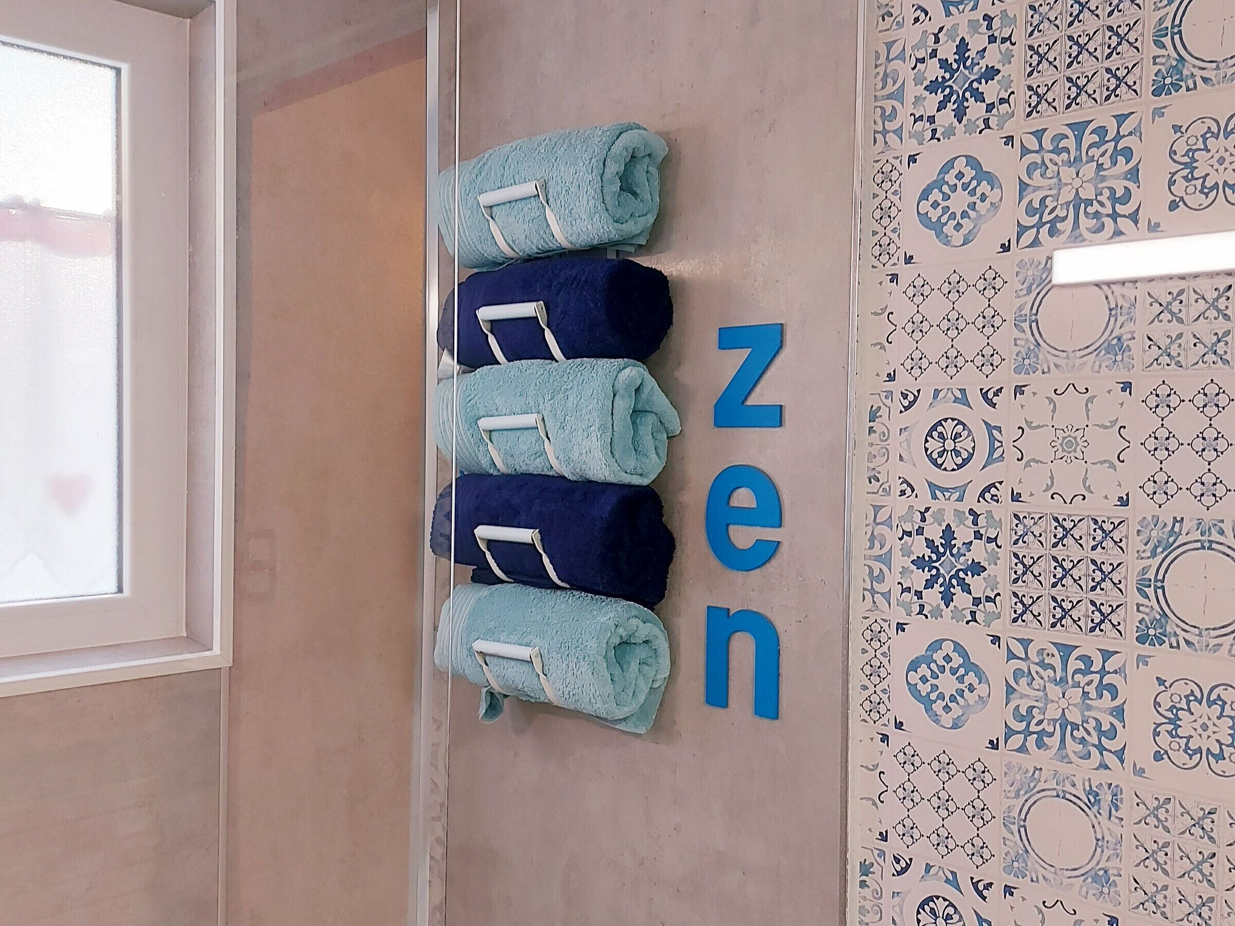 A bathroom with a towel rack holding four towels, a wall with the word "zen" spelled out in large letters, and a patterned tile backsplash.
