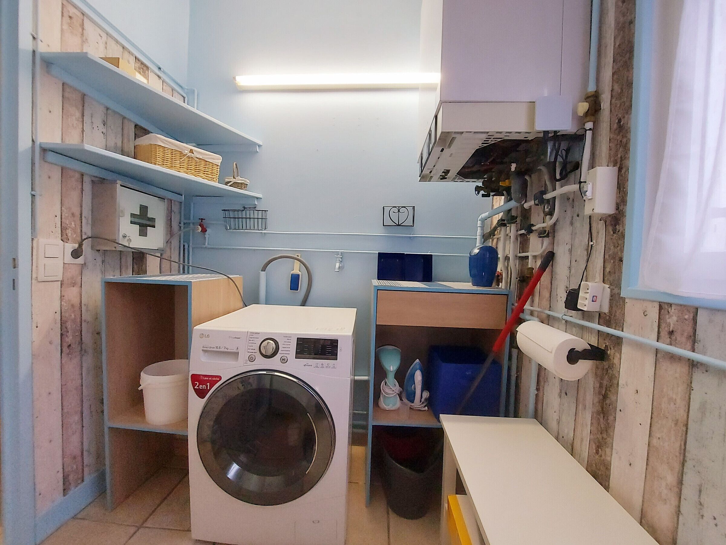 Een praktische wasruimte met een wasmachine, planken met manden, een klein wastafeltje en een afvalbak.