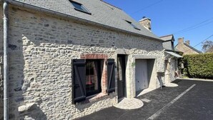 A stone building with a small window and a door, a paved driveway, and a clear blue sky.