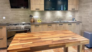 A modern kitchen with wooden cabinets, a built-in stove, and a large wooden table. - La Grange: Comfortable Cottage in Briou, 5 Bedrooms (Briou)