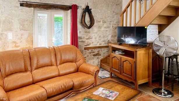A living room with a leather sofa, wooden entertainment unit, TV, and a fan. - La Grange: Comfortable Cottage in Briou, 5 Bedrooms (Briou)