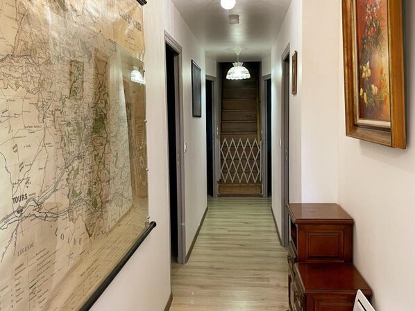Un couloir avec une grande carte accrochée au mur sur la gauche, un meuble en bois sur la droite et une porte au fond.