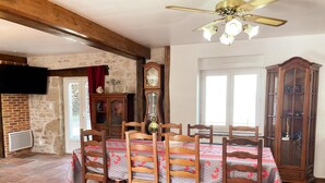 A dining area with a wooden table and chairs, a ceiling fan, a clock, and a brick wall. - La Grange: Comfortable Cottage in Briou, 5 Bedrooms (Briou)