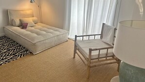 Un dormitorio con cama, una silla, una lámpara y una ventana con cortinas.