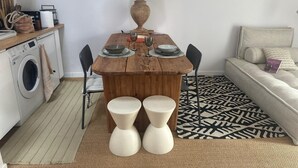 Un espacio habitable pequeño con una mesa de comedor de madera, dos sillas, un sofá, una lavadora y una alfombra estampada.