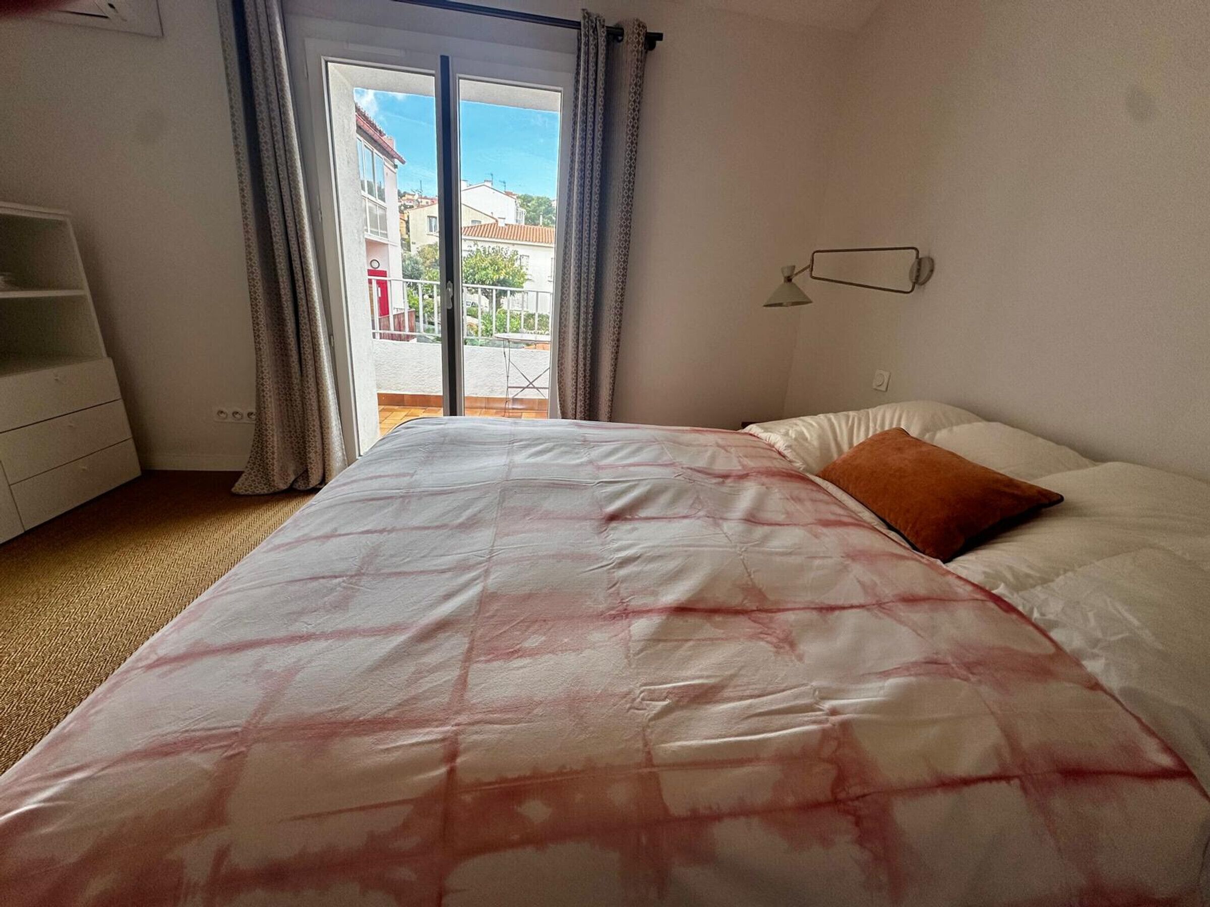Une chambre à coucher avec un lit, une commode, une fenêtre avec des rideaux et une vue sur les bâtiments à l’extérieur.
