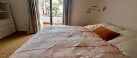 Une chambre à coucher avec un lit, une commode, une fenêtre avec des rideaux et une vue sur les bâtiments à l’extérieur.