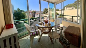 Un balcon avec une table et des chaises, un panier en osier et un panier rouge posé sur une commode blanche.