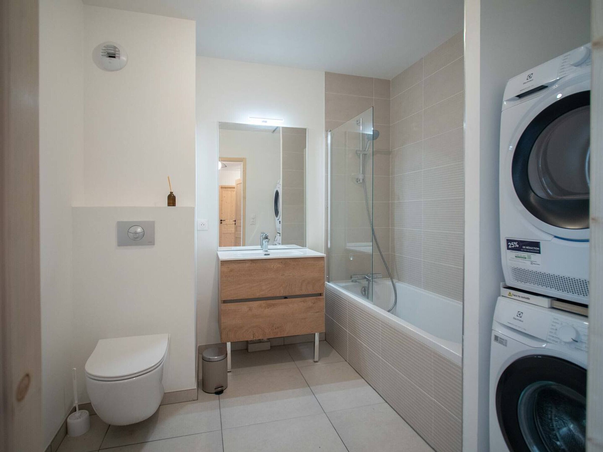 Une petite salle de bain comprenant des toilettes, un lavabo, un miroir et une douche fermée par une paroi de verre.