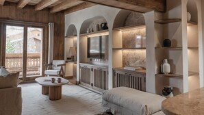Un salon chaleureux avec une cheminée, des poutres apparentes, un coin repas et une vue sur l’extérieur.