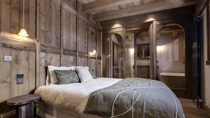 Une chambre à coucher avec une tête de lit en bois, un lit recouvert d’une couvre-lit à motifs gris et blancs, une table de chevet et un miroir.