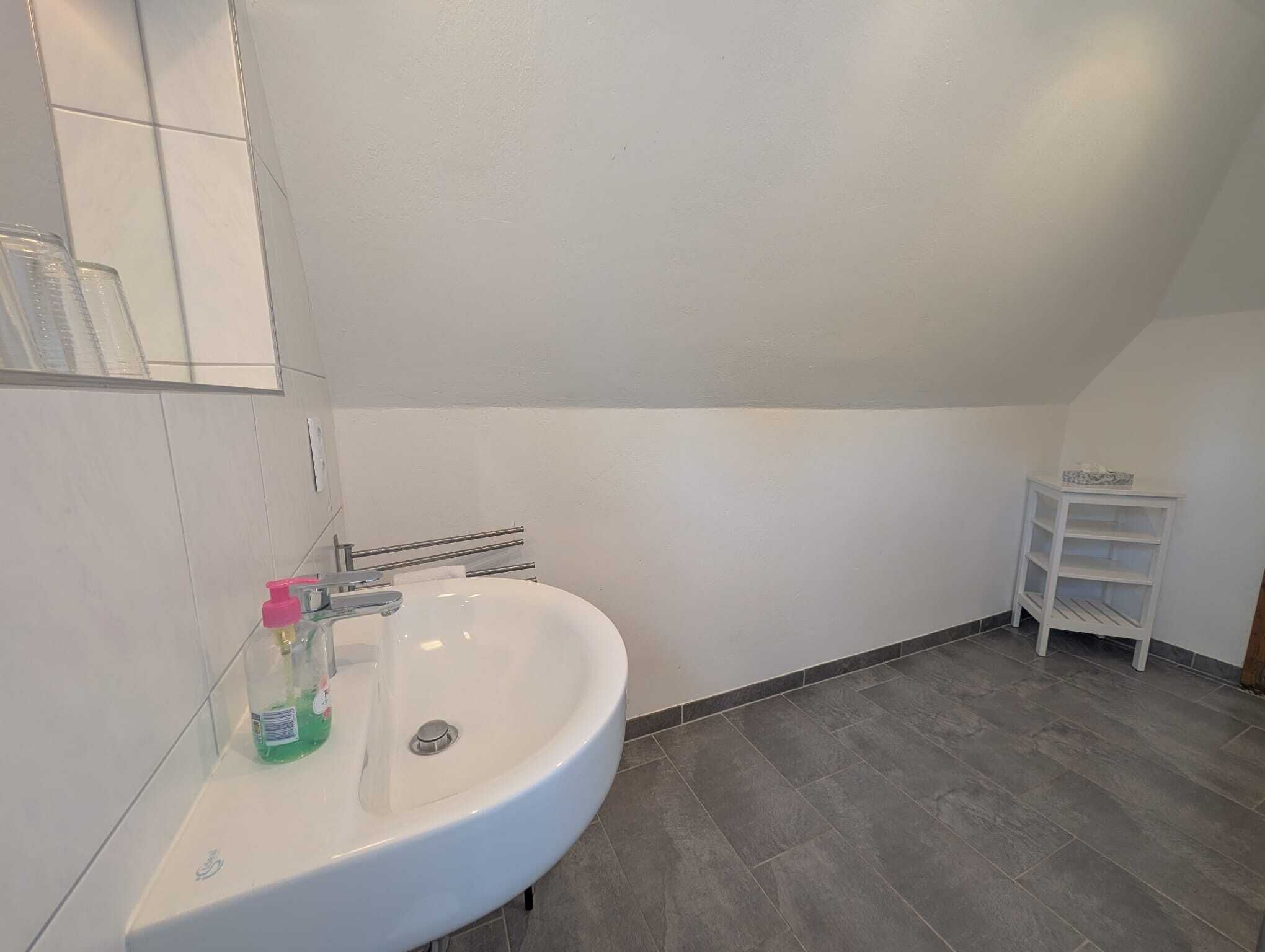 A modern bathroom with a white sink, a mirror, and a small white shelf.