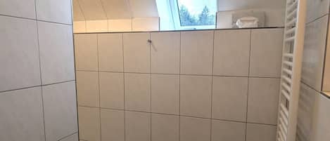 Uma casa de banho com azulejos brancos, uma janela, um porta-toalhas e uma pia com dispensador de sabonete.