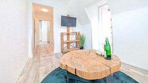 A modern living room with a round wooden coffee table, a flat-screen TV mounted on the wall, and a potted plant. - Harzlodge Hilly – Your Private Family Holiday Apartment in the Harz Mountains (Braunlage)