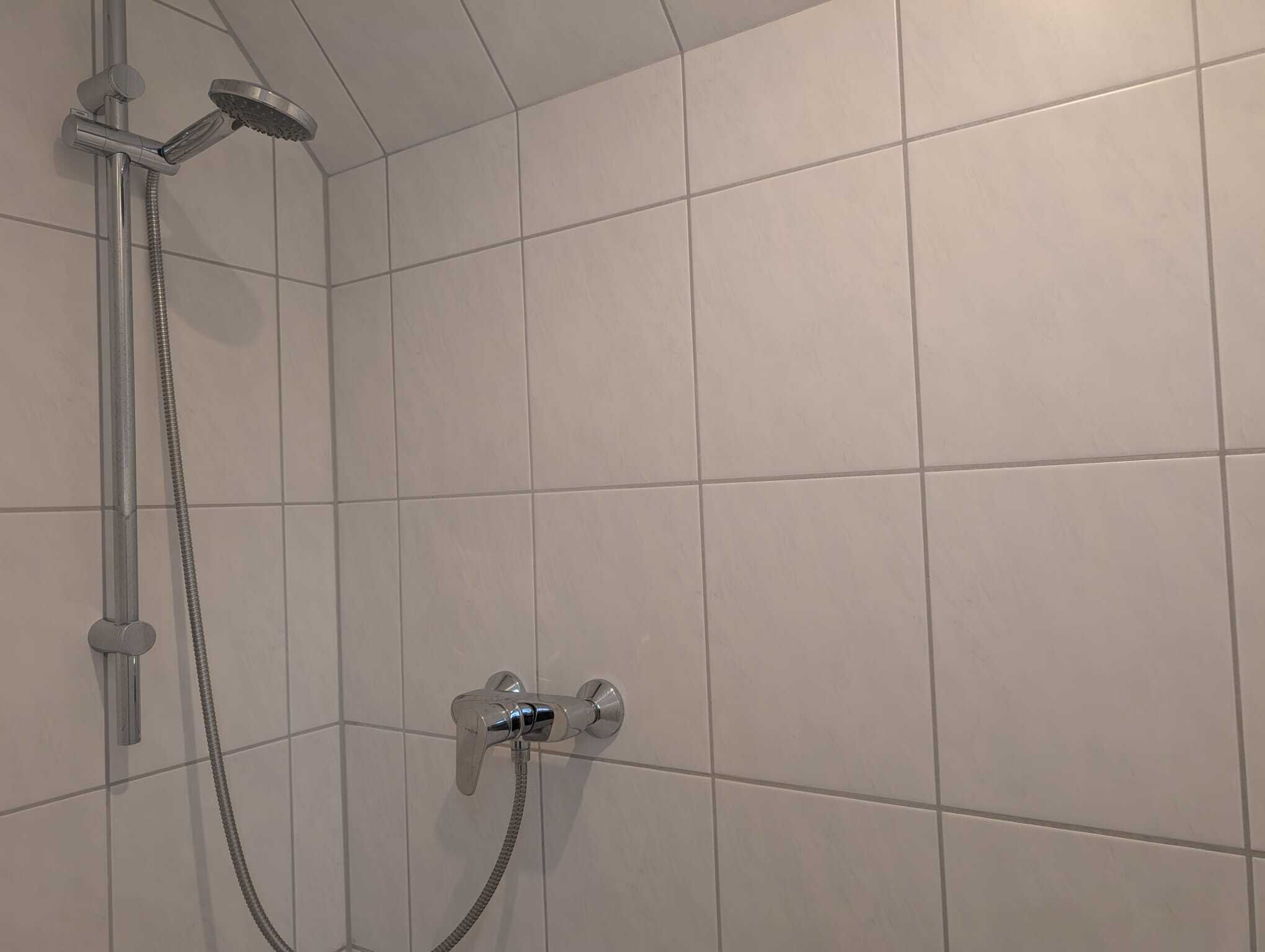 Ein Duschbereich mit Handbrause und am Wand montiertem Wasserhahn.