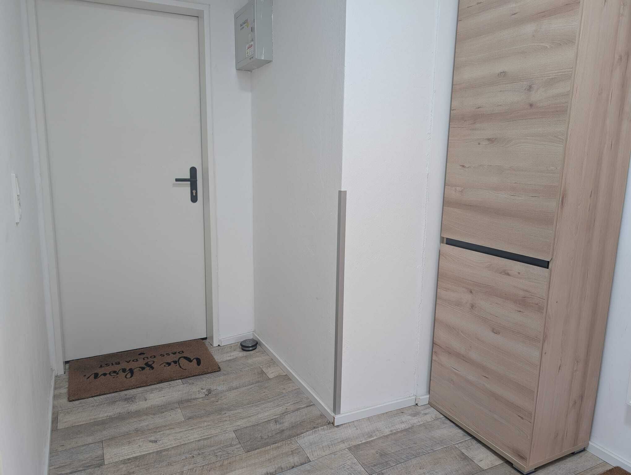 Een gang met een witte deur, een houten kast en een deurmat met tekst.