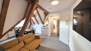 A cozy loft apartment with exposed wooden beams, a dining area with a table and chairs, a sofa, and a kitchen in the background. - Harzlodge Hilly – Your Private Family Holiday Apartment in the Harz Mountains (Braunlage)