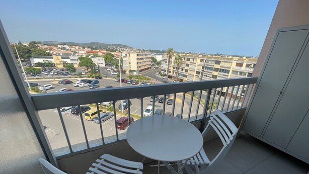 A balcony with a table and two chairs, overlooking a parking lot and buildings. - 2-star apartment near thermal baths with balcony (Balaruc-les-Bains)