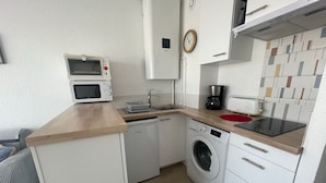 A compact kitchen with a microwave, coffee maker, toaster, and washing machine. - 2-star apartment near thermal baths with balcony (Balaruc-les-Bains)