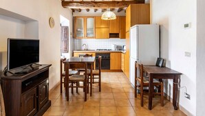 A compact kitchen with wooden cabinets, a dining table, and a TV. - GuestHost - Battazzi House (Peglio)