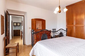 A bedroom with a bed, a wooden wardrobe, a chair, and a hallway leading to a bathroom.