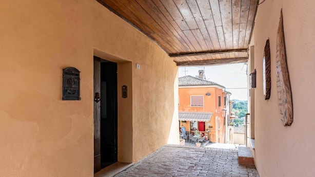 A narrow cobblestone alleyway with a wooden ceiling, a door on the left, and a building with a tiled roof in the background. - GuestHost - Battazzi House (Peglio)