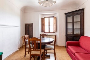 A dining area with a round table, wooden chairs, a red sofa, and a dark wooden cabinet.