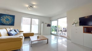 Una sala de estar moderna con sofá, mesa de centro, televisor y puerta corredera de vidrio que da a un espacio exterior.