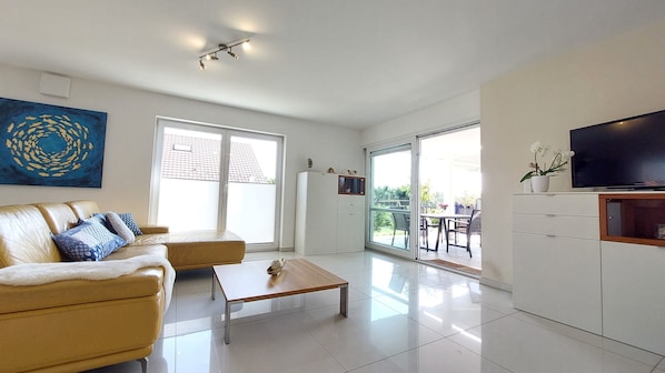 A modern living room with a sofa, coffee table, TV, and a sliding glass door leading to an outdoor area.