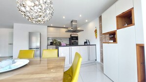 Una cocina moderna con gabinetes blancos, un extractor de acero inoxidable y un comedor con mesa de madera y sillas amarillas.