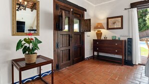 Une pièce avec une porte en bois, un miroir, une table avec une plante, une commode et un haut-parleur.