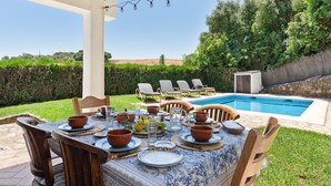 Un espace extérieur aménagé pour les repas, avec une piscine, des chaises en bois et une table dressée pour un repas.